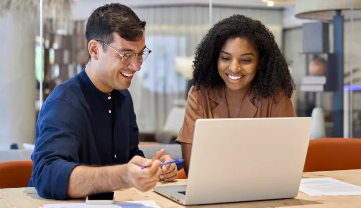 The best hotel management system features for independent hotels - A man and a woman work on a computer in a hotel lobby while smiling - Hospitality Solutions