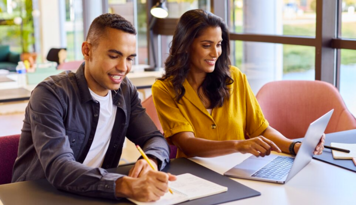 Boost hotel revenue with smart gift card solutions - A man and a woman sit at a table looking at a computer and writing on a notepad - Hospitality Solutions