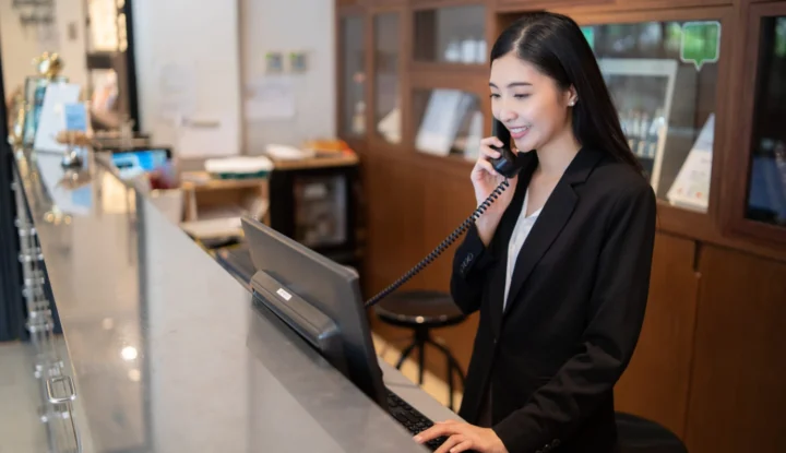 The importance of the hotelier's role in maximizing revenue - A front desk associate smiles and answers the phone - Sabre Hospitality