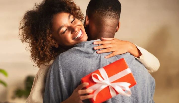 Top features of a hotel gift card system management platform - A woman hugs a man, holding a red wrapped present and smiling - Sabre Hospitality