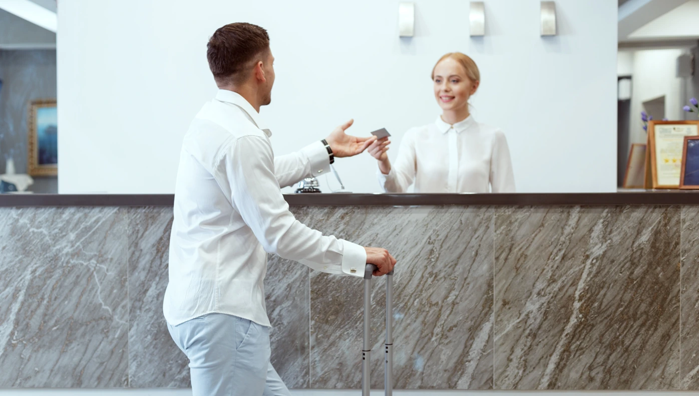 Top features to look for in a hotel management system - Man recieves his room key at a hotel from the smiling front desk associate - Sabre Hospitality