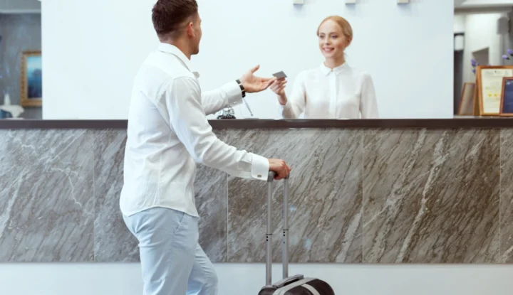 Top features to look for in a hotel management system - A male guest at a hotel receives his room key from a smiling front desk associate - Sabre Hospitality
