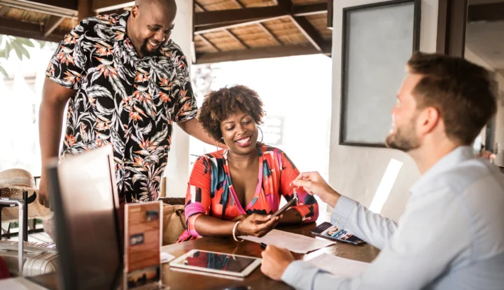 The best hotel management systems for independent hotels in 2025 - Two guests smile, talking to a front desk consultant at a hotel - Sabre Hospitality